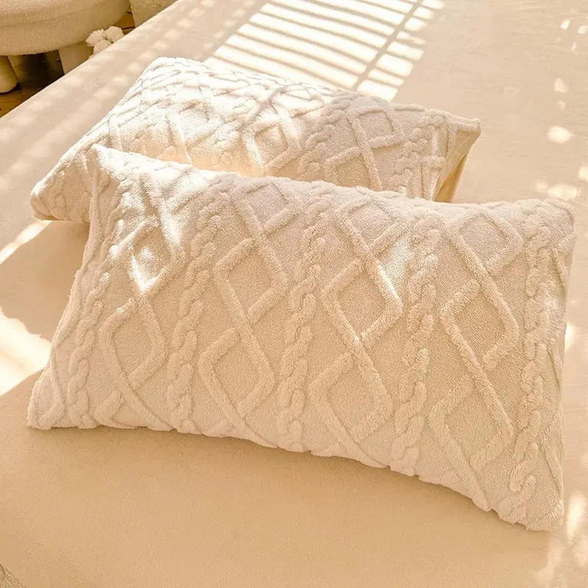 Two cream textured velvet pillowcases with a diamond and cable knit pattern on a bed.