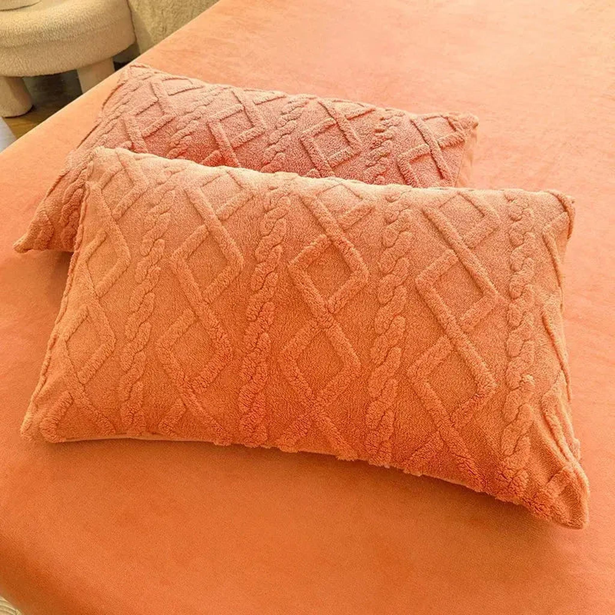 Two peach-colored textured velvet pillowcases with a diamond and braid pattern on a bed.