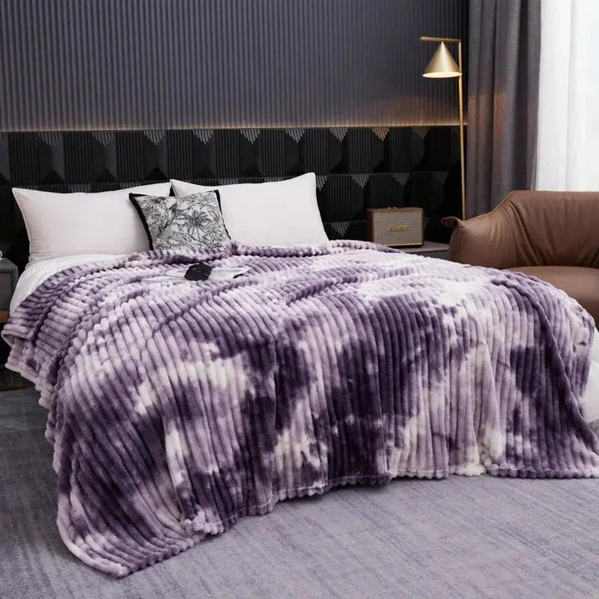 Plush purple and white tie-dye flannel fleece blanket draped on a bed, showcasing its soft, ribbed texture.