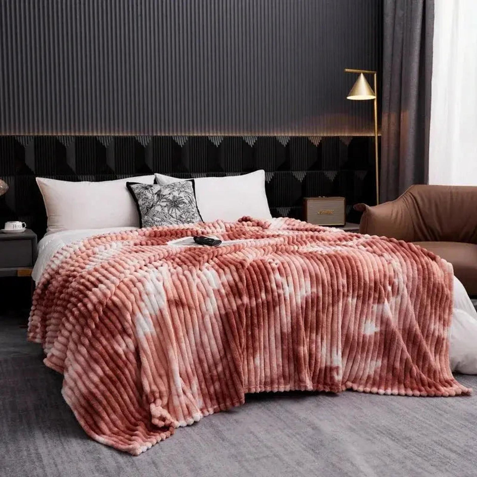 Pink and white tie-dye flannel fleece blanket with a ribbed texture draped on a bed.