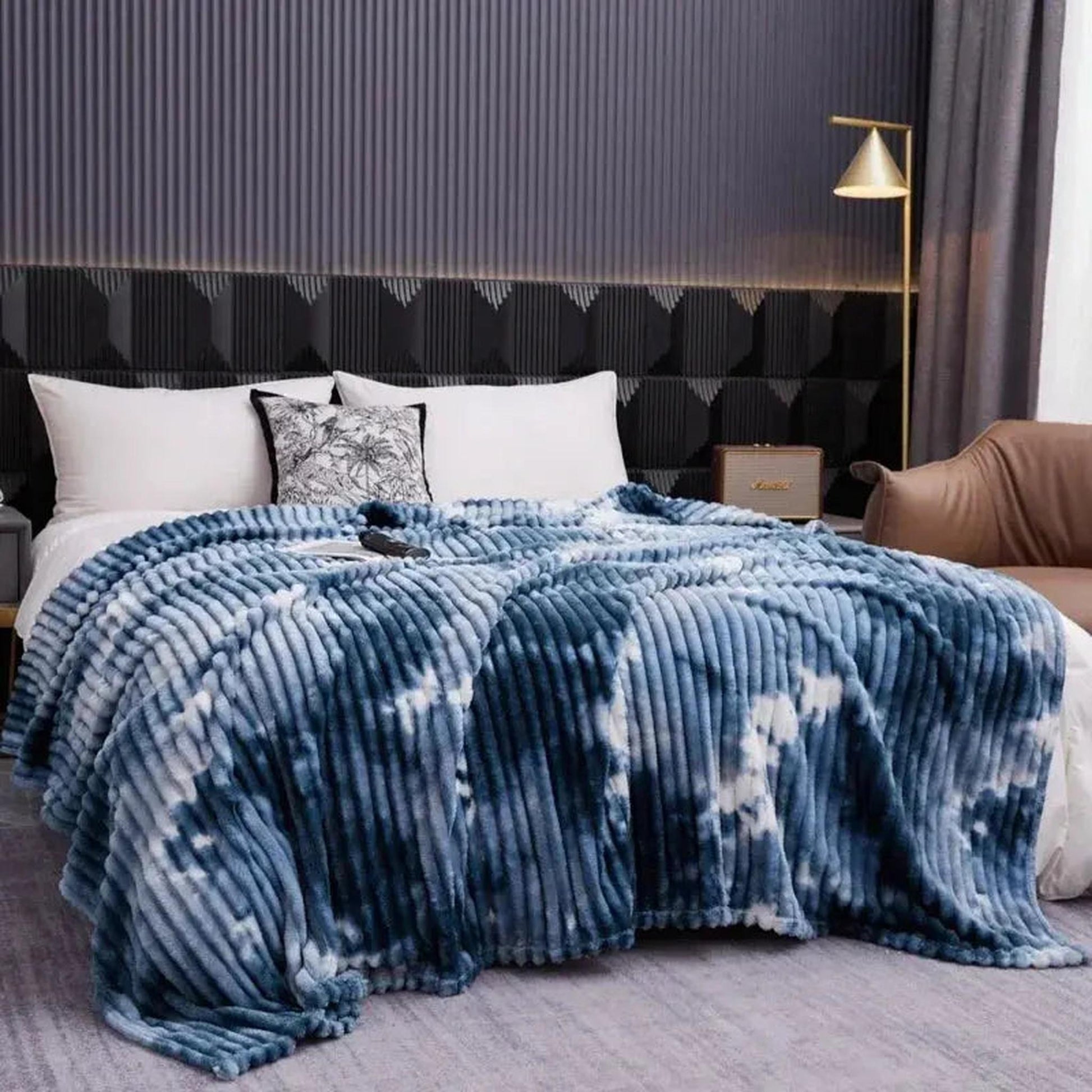 Blue and white tie-dye flannel fleece blanket with a ribbed texture draped on a bed.