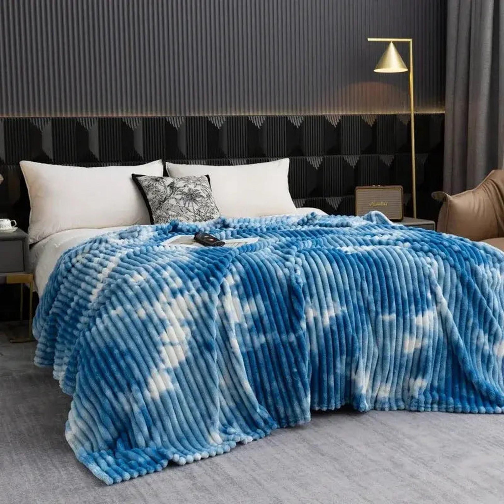 Blue and white tie-dye flannel fleece blanket with a ribbed texture draped on a bed.