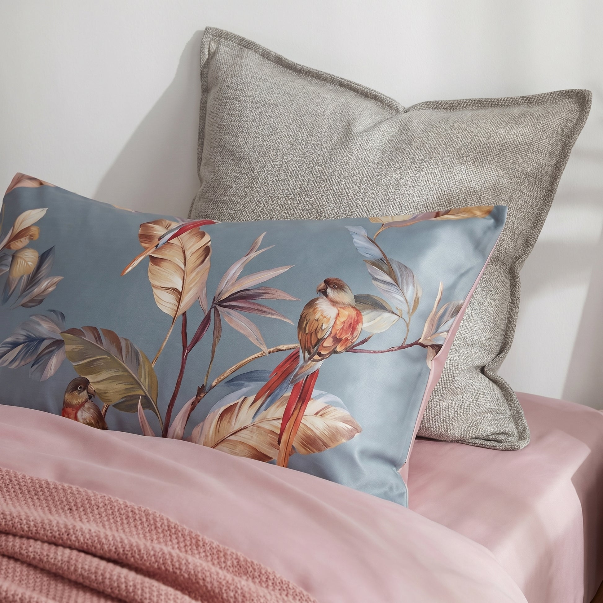 Tropical Parrots Bedding Set with blue-grey pillowcase, vibrant parrot illustrations, warm-toned leaves, and dusty pink edges.