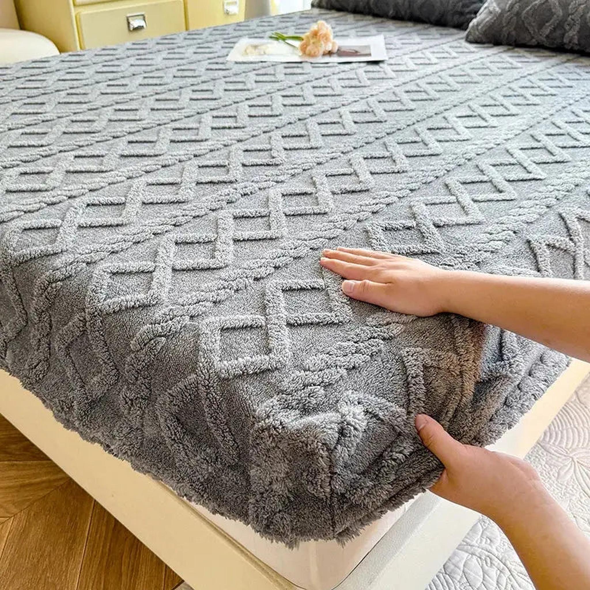 Hands adjusting a gray, textured coral fleece fitted bed sheet with a geometric diamond pattern.