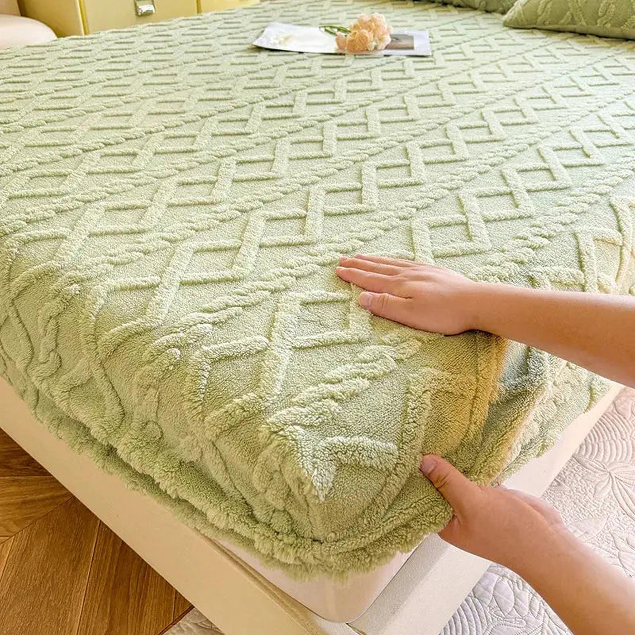 Hands adjusting a light green, textured coral fleece fitted bed sheet with a geometric pattern.