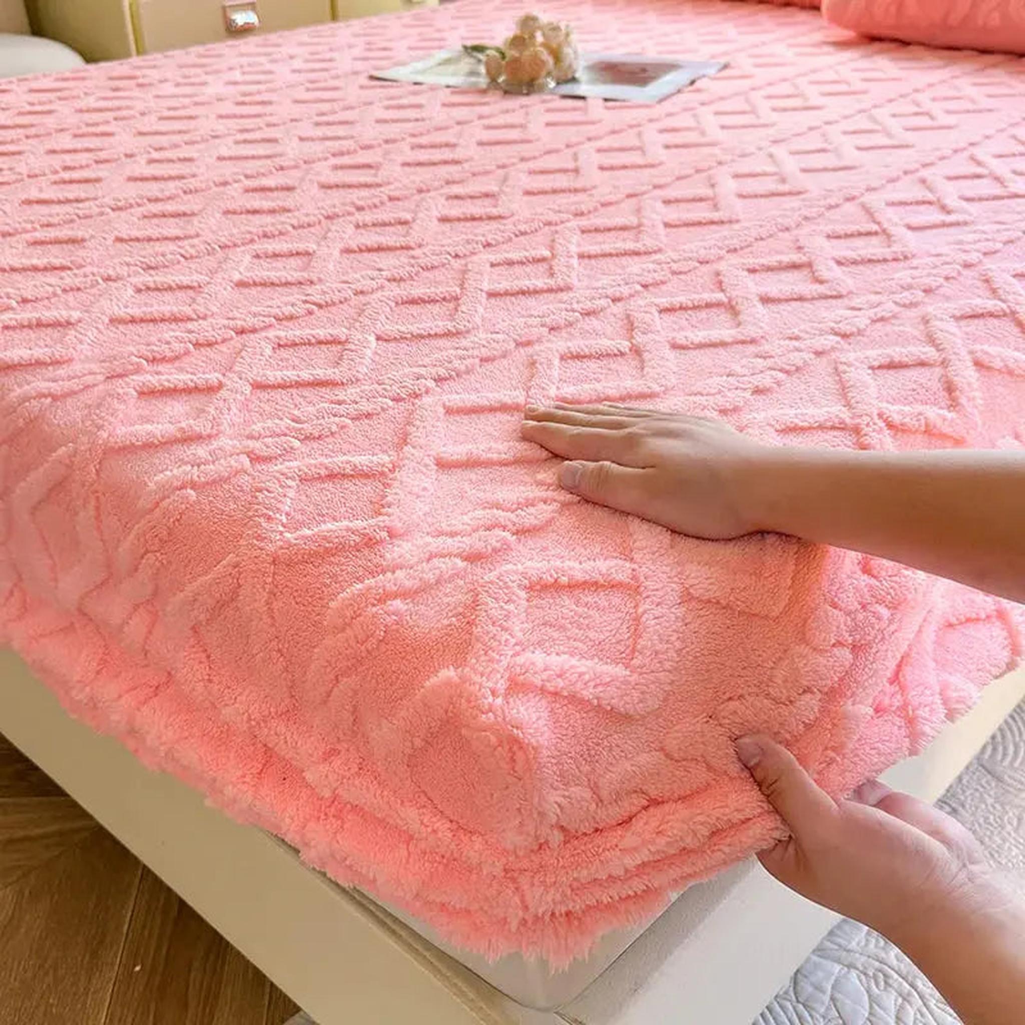 Pink coral fleece fitted bed sheet with a textured ribbed pattern, being smoothed by hands.