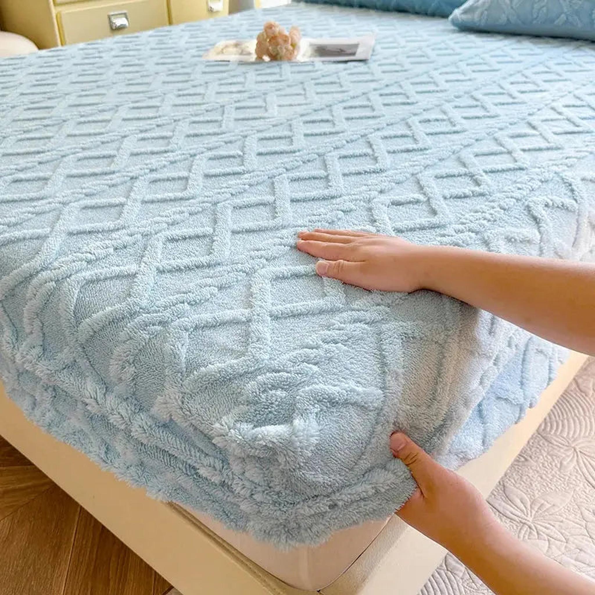 Hands adjusting a light blue, textured coral fleece fitted bed sheet with a geometric pattern.