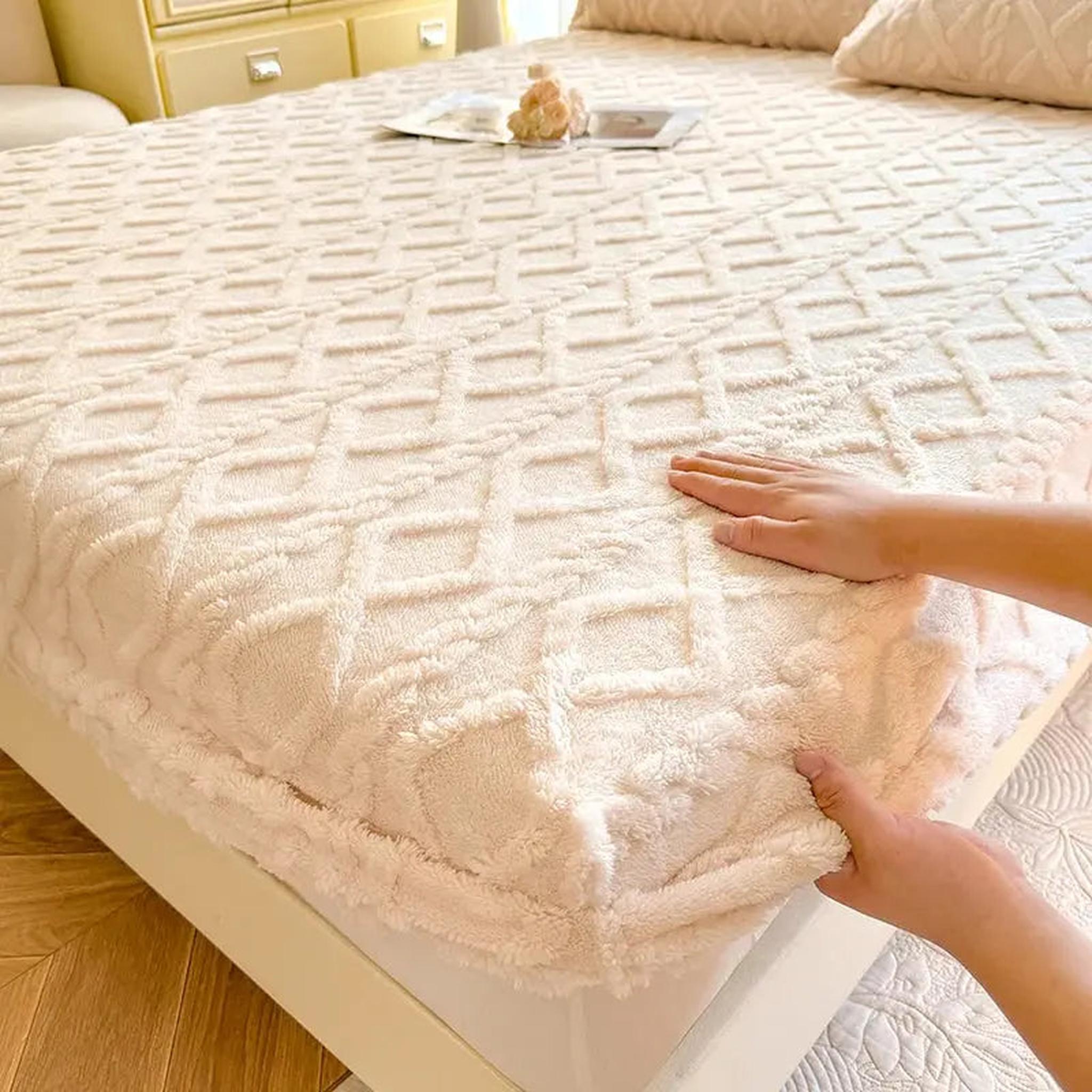 Hands adjusting a cream-colored, textured coral fleece fitted bed sheet with a diamond pattern.