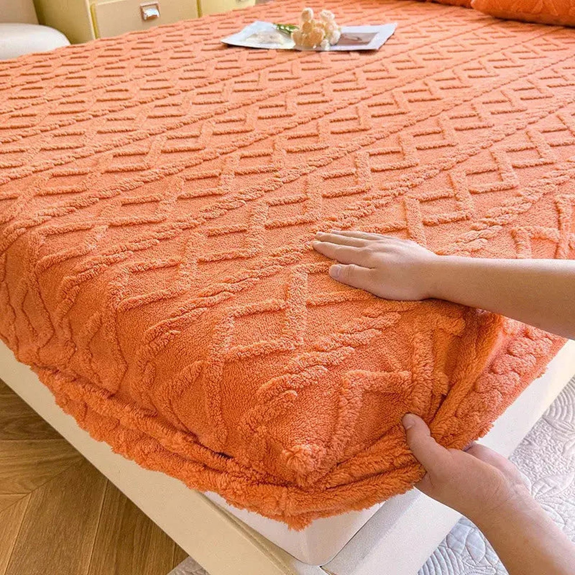 Warm coral fleece fitted bed sheet with a textured ribbed pattern, shown being adjusted on a mattress.