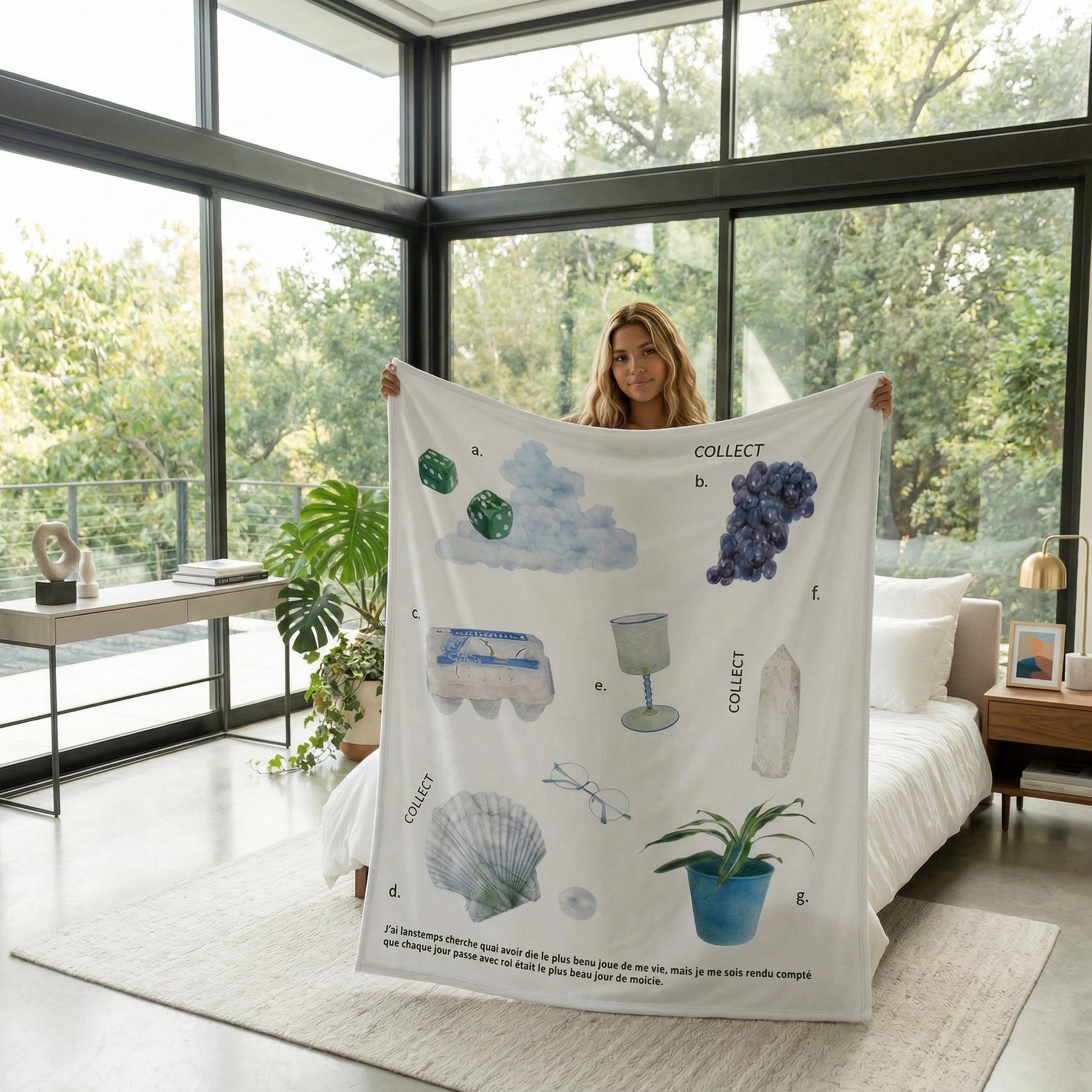 Woman holding a white Vikama Flannel Blanket with a "Collect" design featuring illustrations of dice, grapes, eggs, a shell, and a plant.