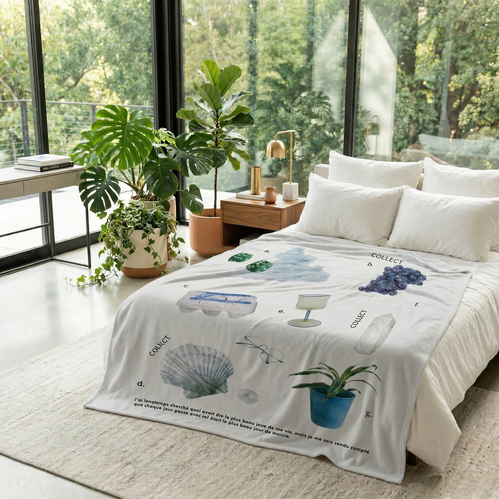Vikama Flannel Blanket, white with "Collect" text and various illustrated items, draped over a white bed in a modern room.