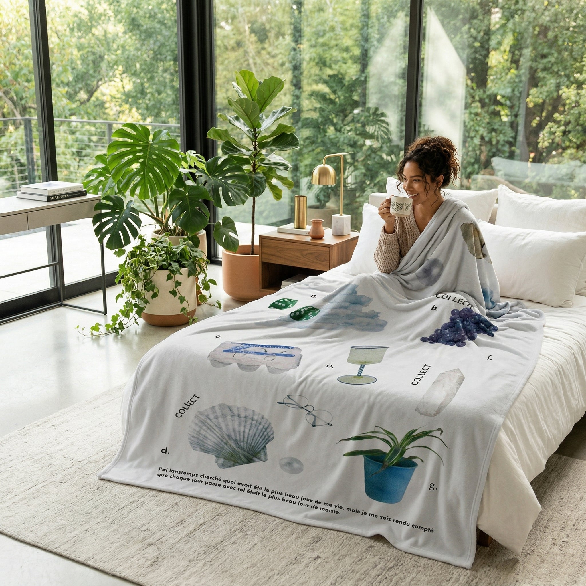 Woman relaxing in bed with a light grey Vikama Flannel Blanket featuring various illustrated objects and text.