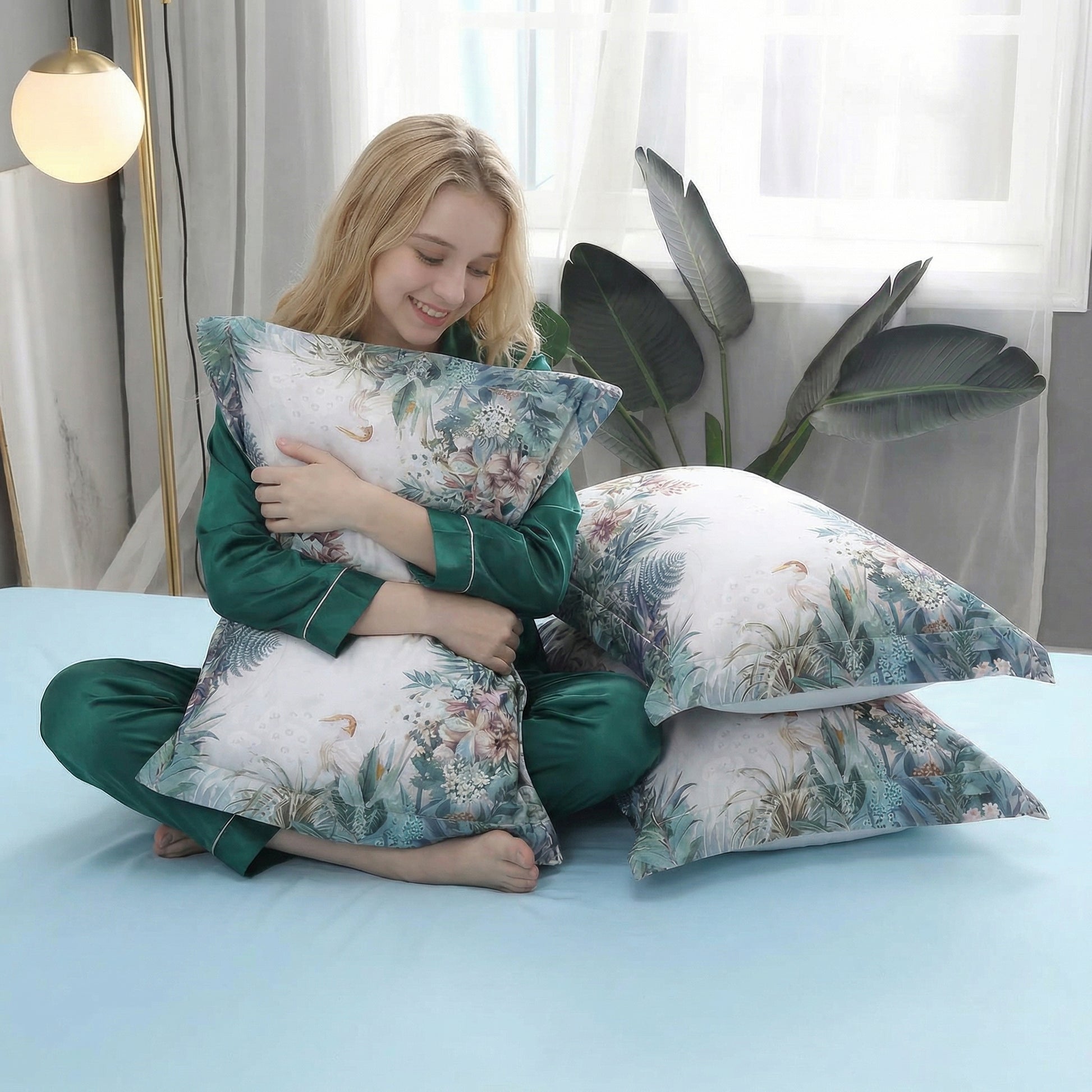 Smiling woman in green pajamas hugging a cotton pillow with a delicate violet floral pattern on a misty grey backdrop.