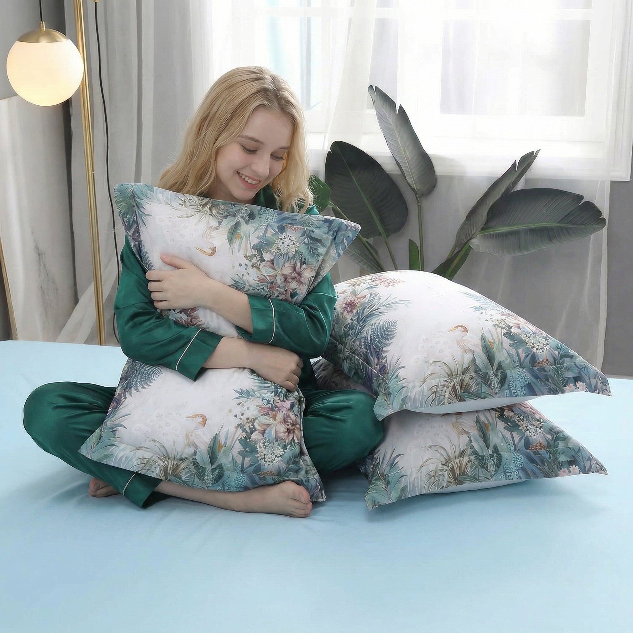 Smiling woman in green pajamas hugging a cotton pillow with a delicate violet floral pattern on a misty grey backdrop.