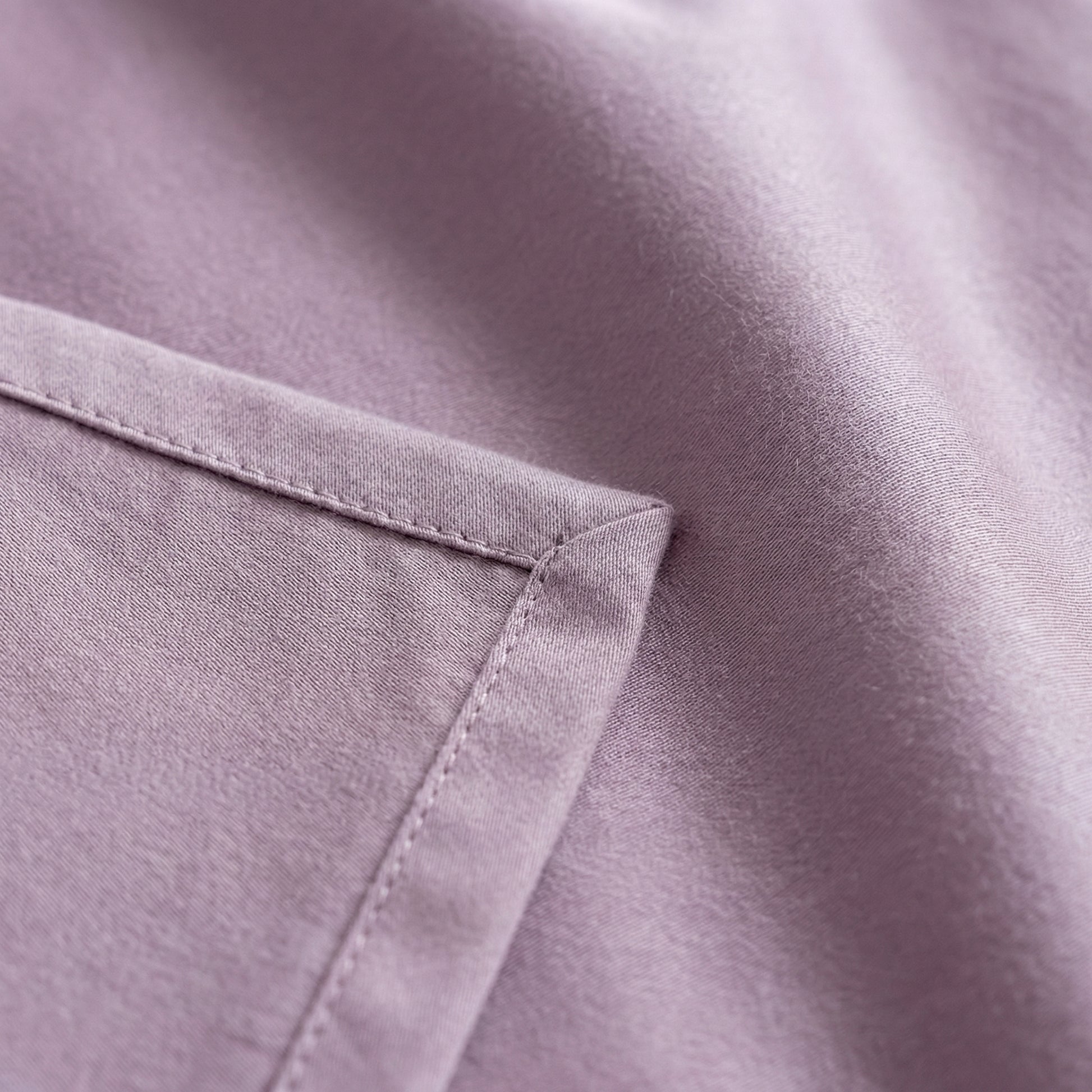 Close-up of a muted violet silk bedding set with a satin finish and stitched corner detail.