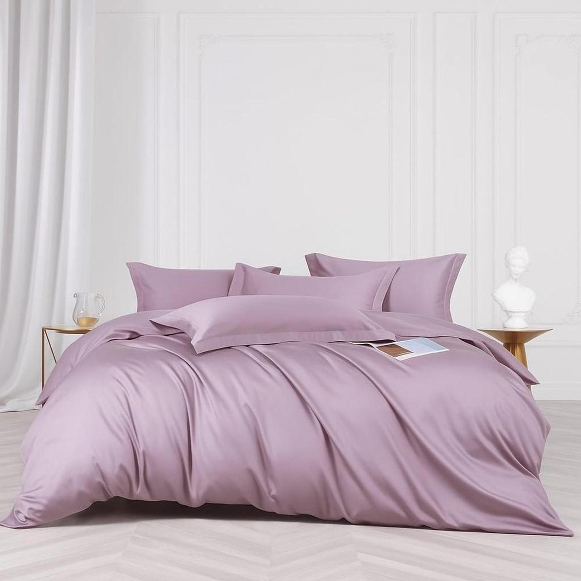Muted violet silk minimalist bedding set with satin finish, duvet cover, and four pillows on a bed.