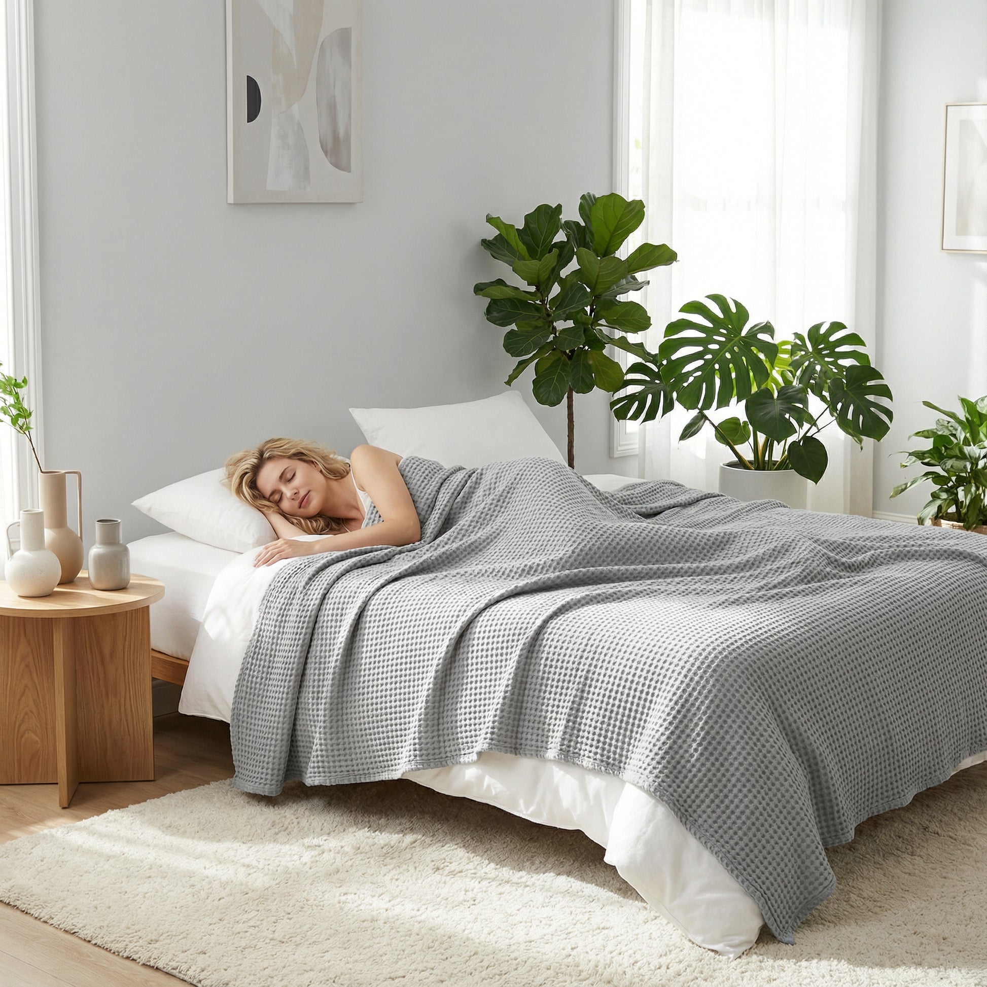 Woman sleeping under a light gray waffle texture cotton blanket on a bed.