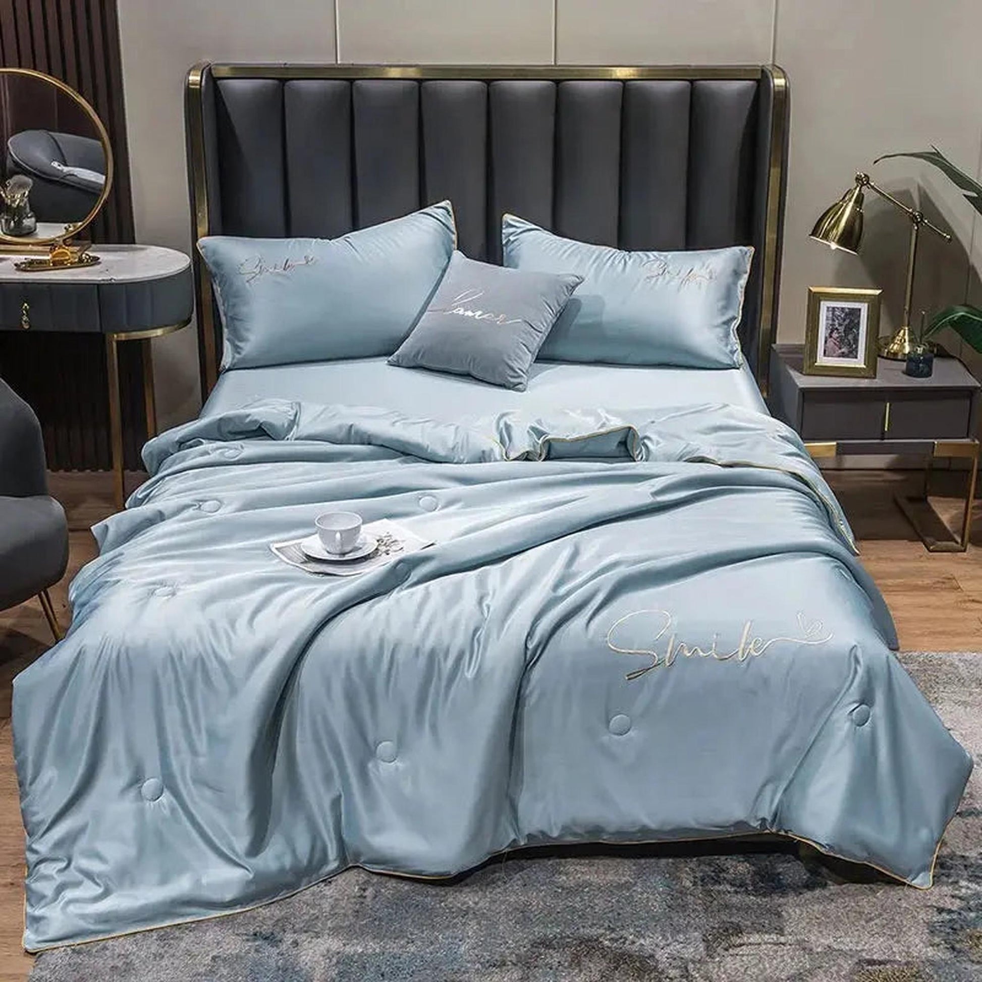 Light blue washed silk summer quilt set with embroidered "Smile" text and gold trim on a modern bed.