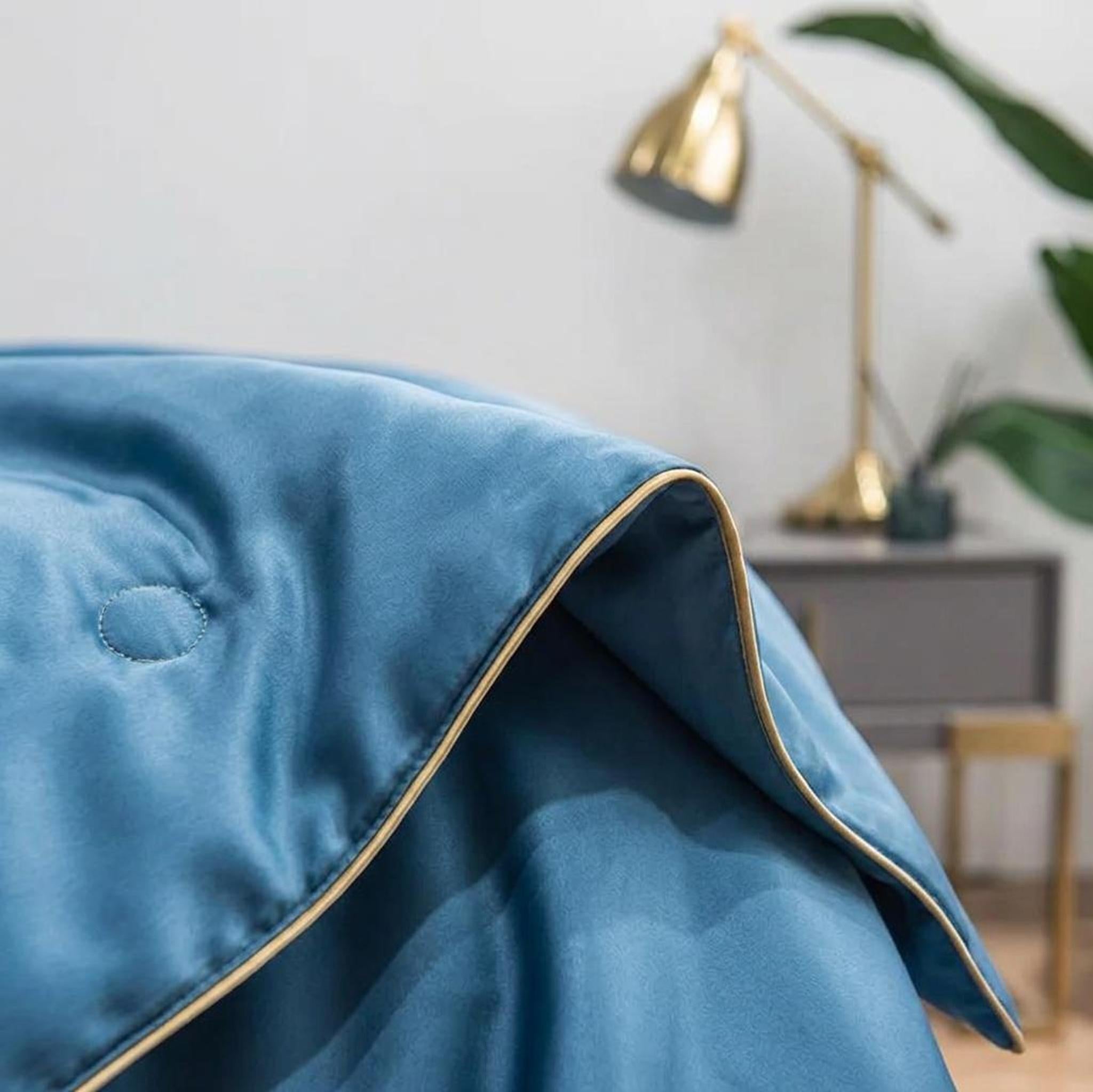 Blue washed silk summer quilt with gold piping and subtle embroidery, draped over a bed.