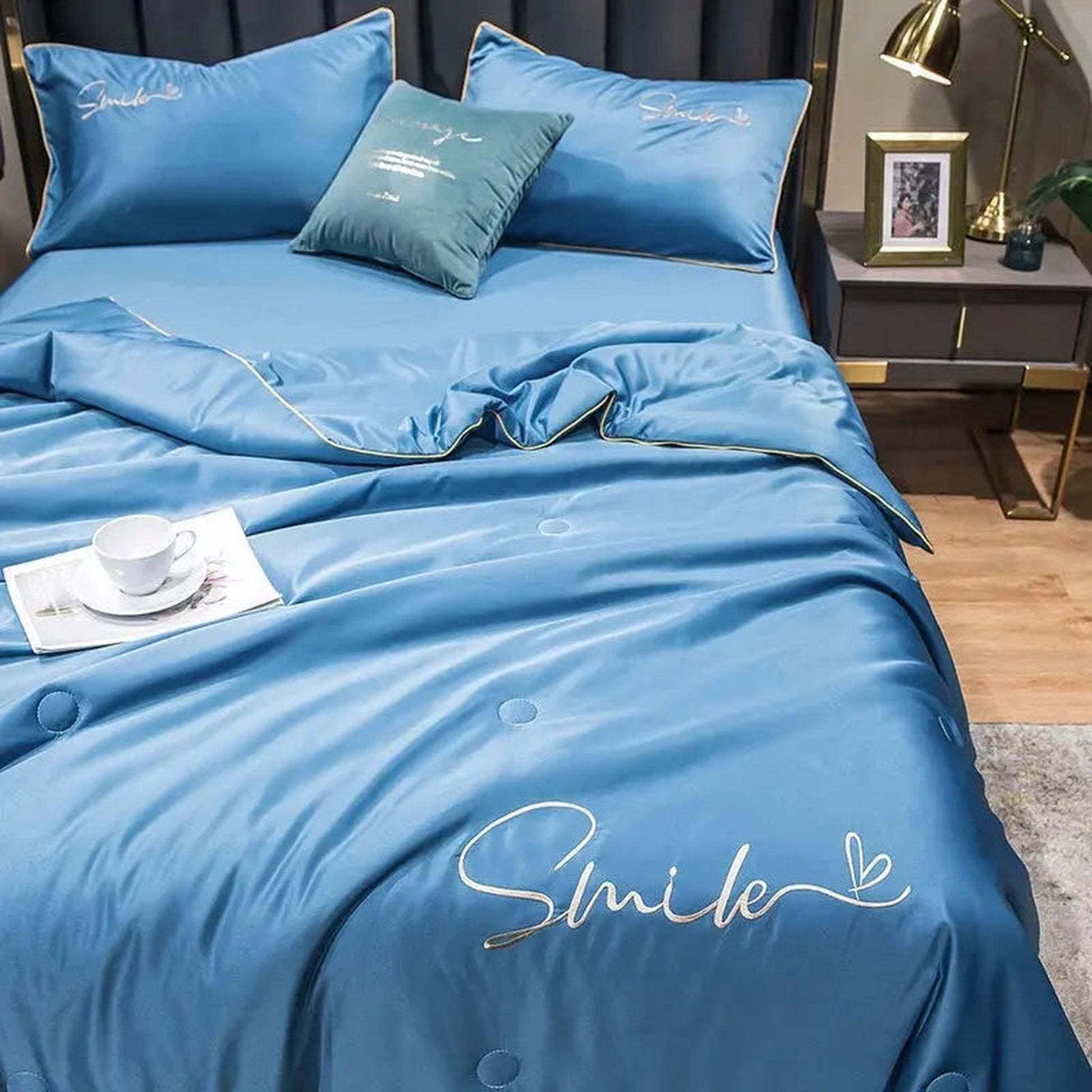 Blue washed silk summer quilt set with "Smile" embroidery and gold piping on a bed.