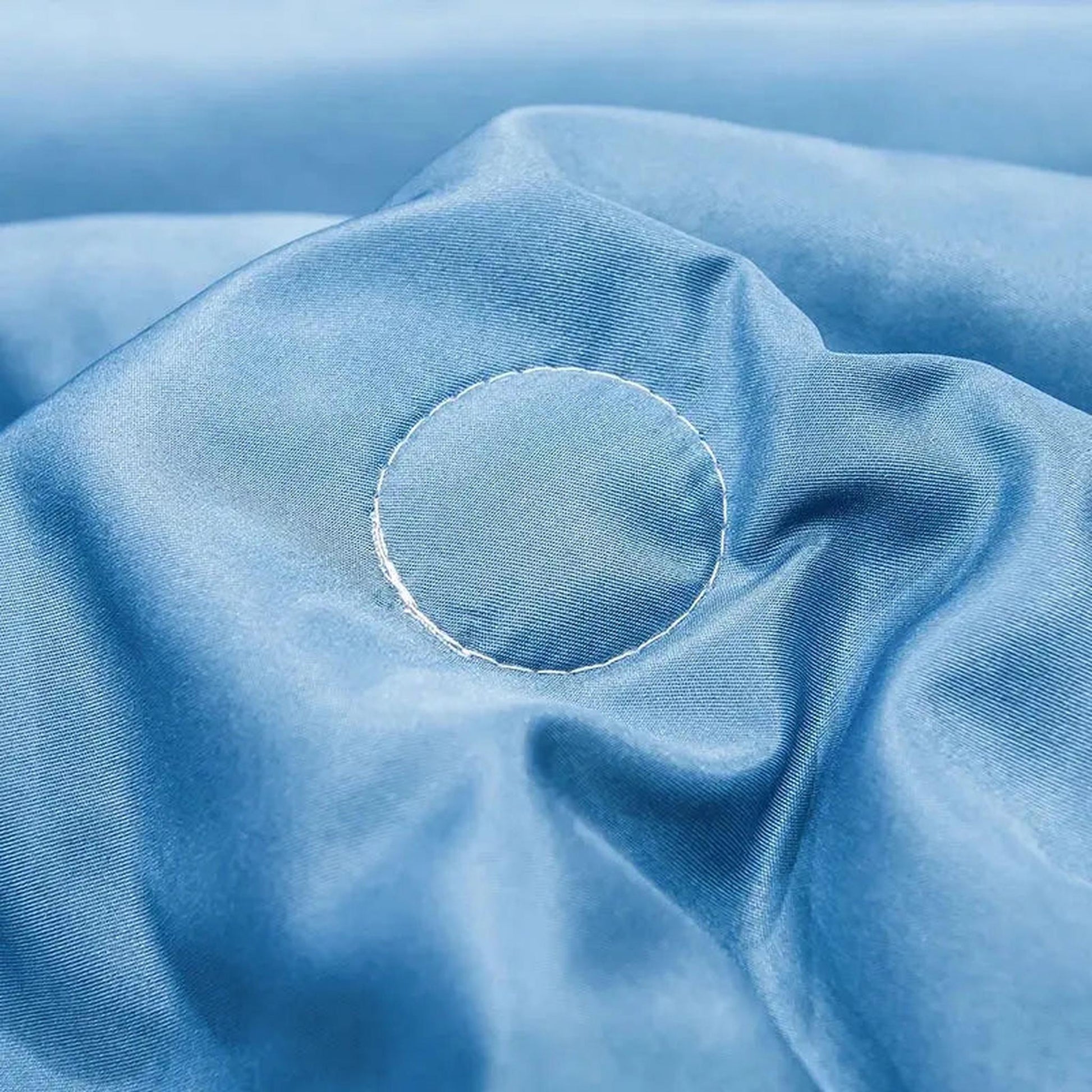 Close-up of a light blue washed silk quilt with subtle white circular embroidery.