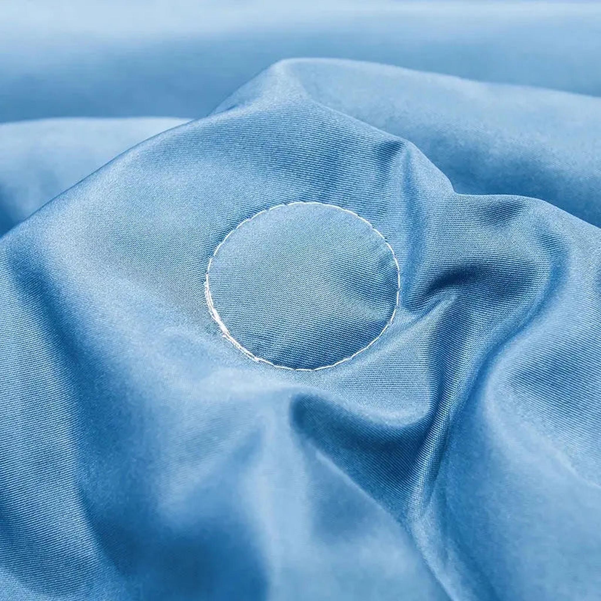 Close-up of a light blue washed silk quilt with subtle white circular embroidery.