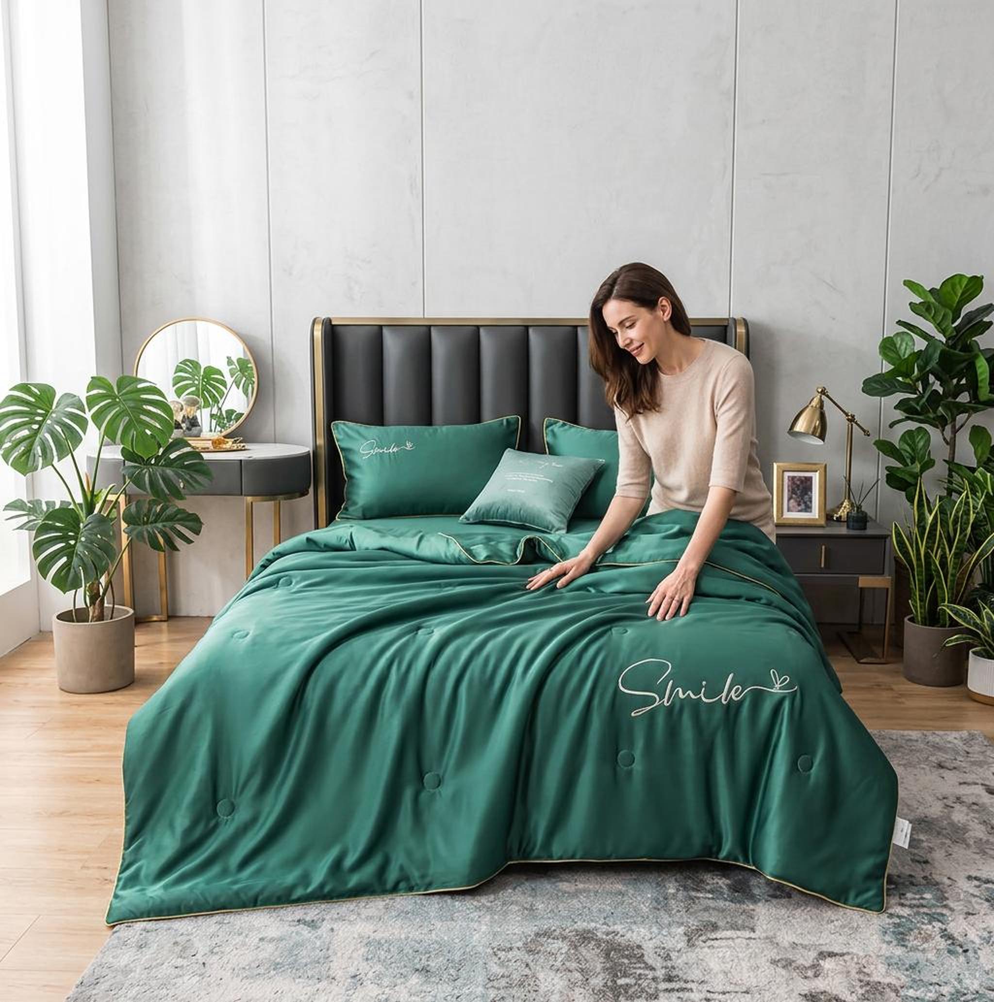 Woman on a bed with a dark green washed silk quilt set, featuring "Smile" embroidery and gold trim.