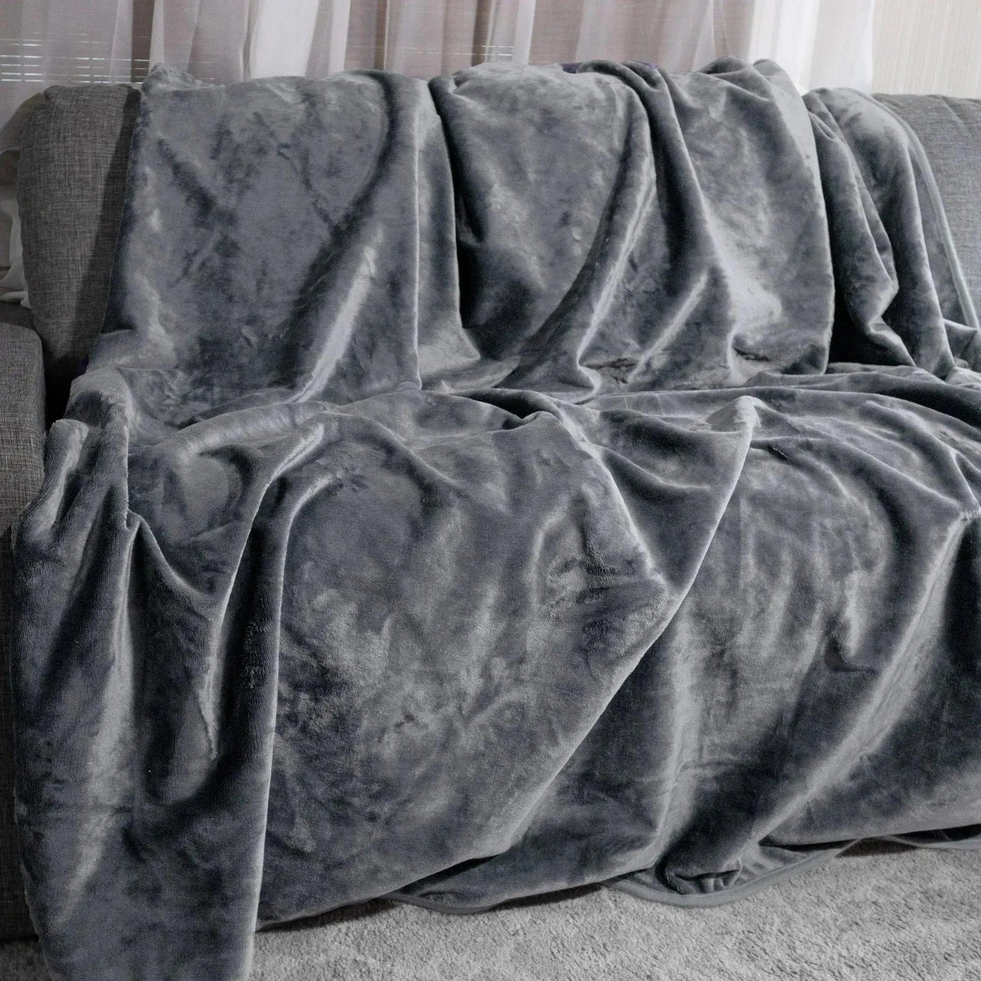 Dark moon grey reversible flannel fleece blanket draped over a grey couch.