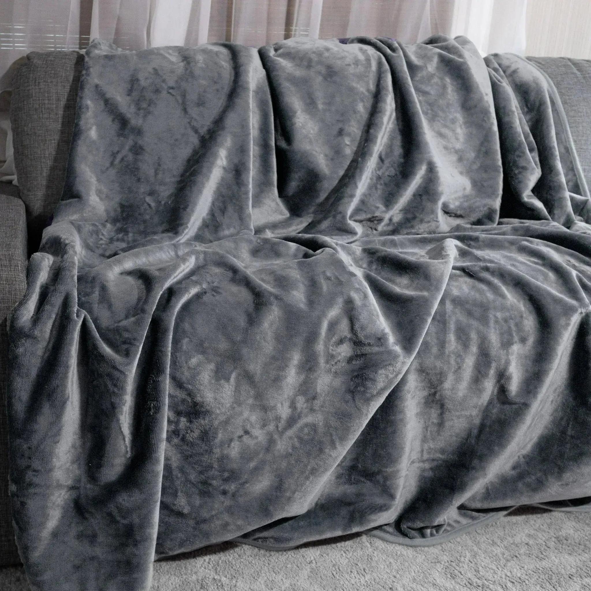 Dark moon grey reversible flannel fleece blanket draped over a grey couch.