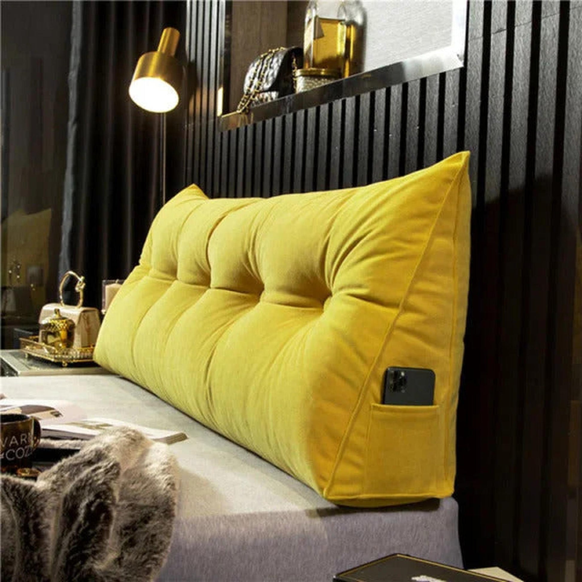 Yellow wedge pillow with tufted design and side pocket for phone, on a bed.