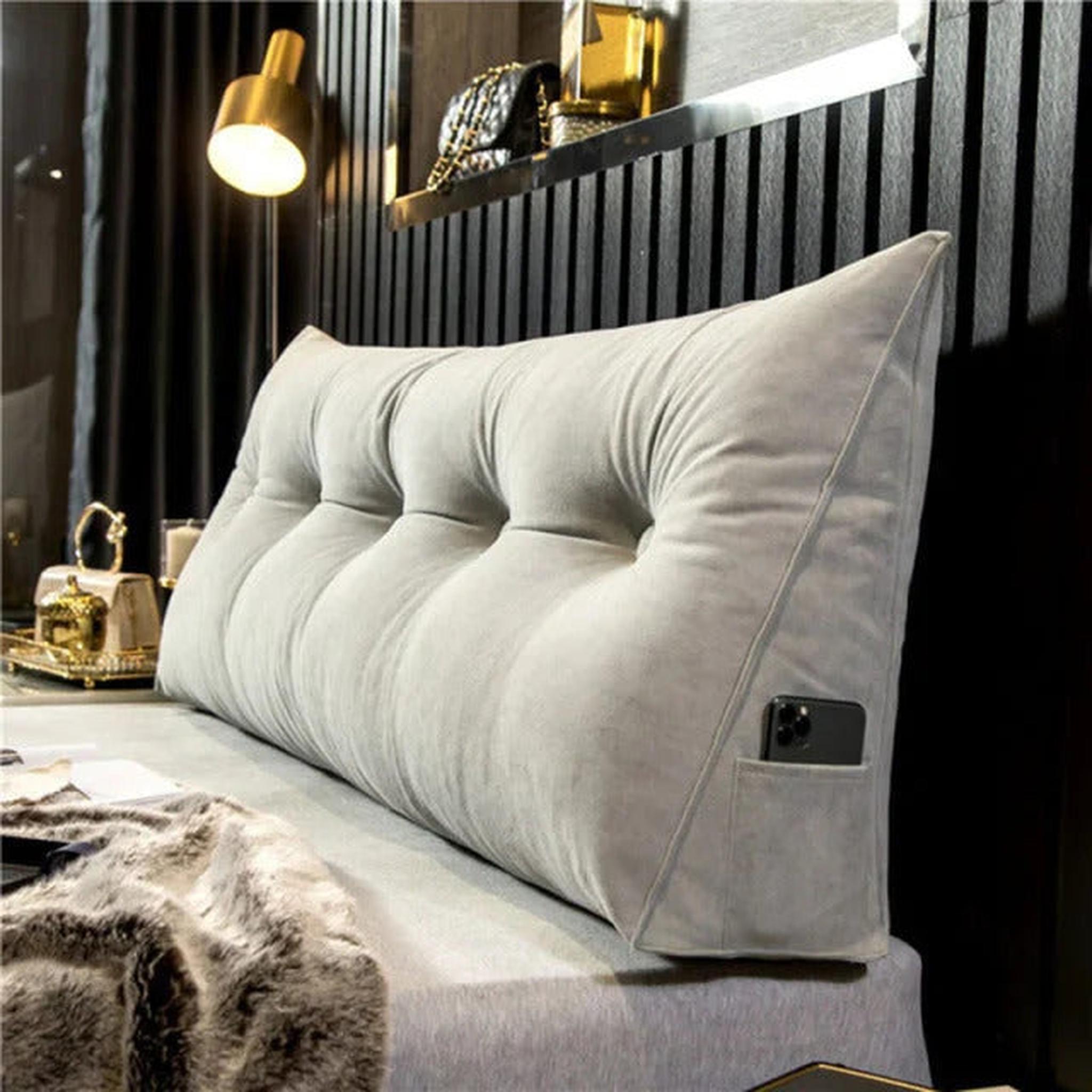 Light gray tufted wedge pillow with side pocket holding a phone, on a bed.