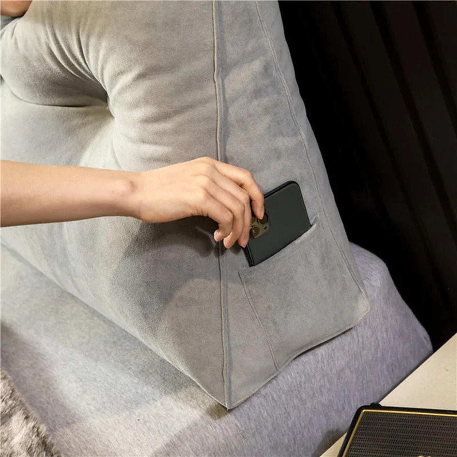 Gray wedge pillow with a side pocket, a hand placing a phone in it.