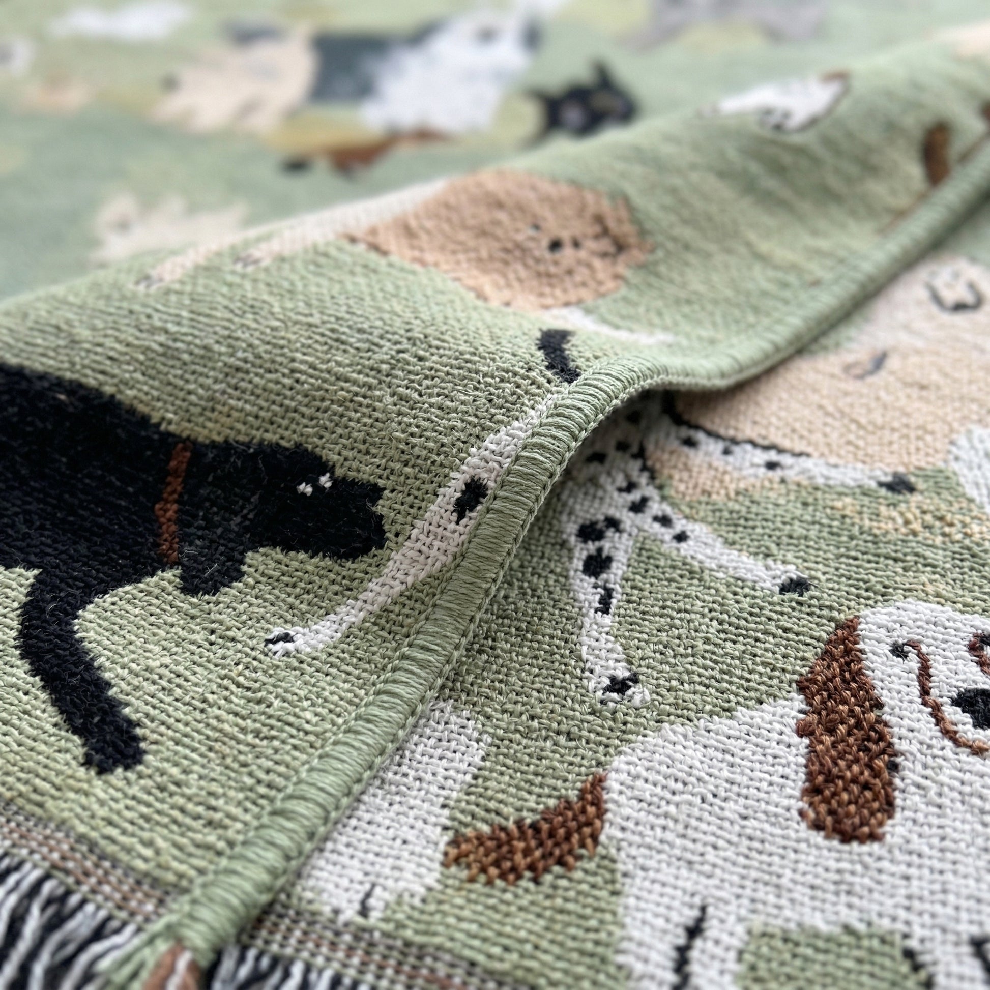 Woven green blanket with playful cartoon dog pattern, featuring black, white, and brown dogs.