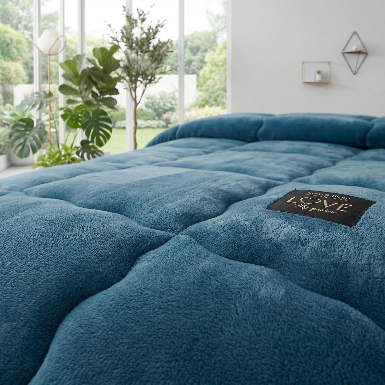 Soft teal quilted polyester blanket with "Love & Sleep" patch, on a bed in a bright room.