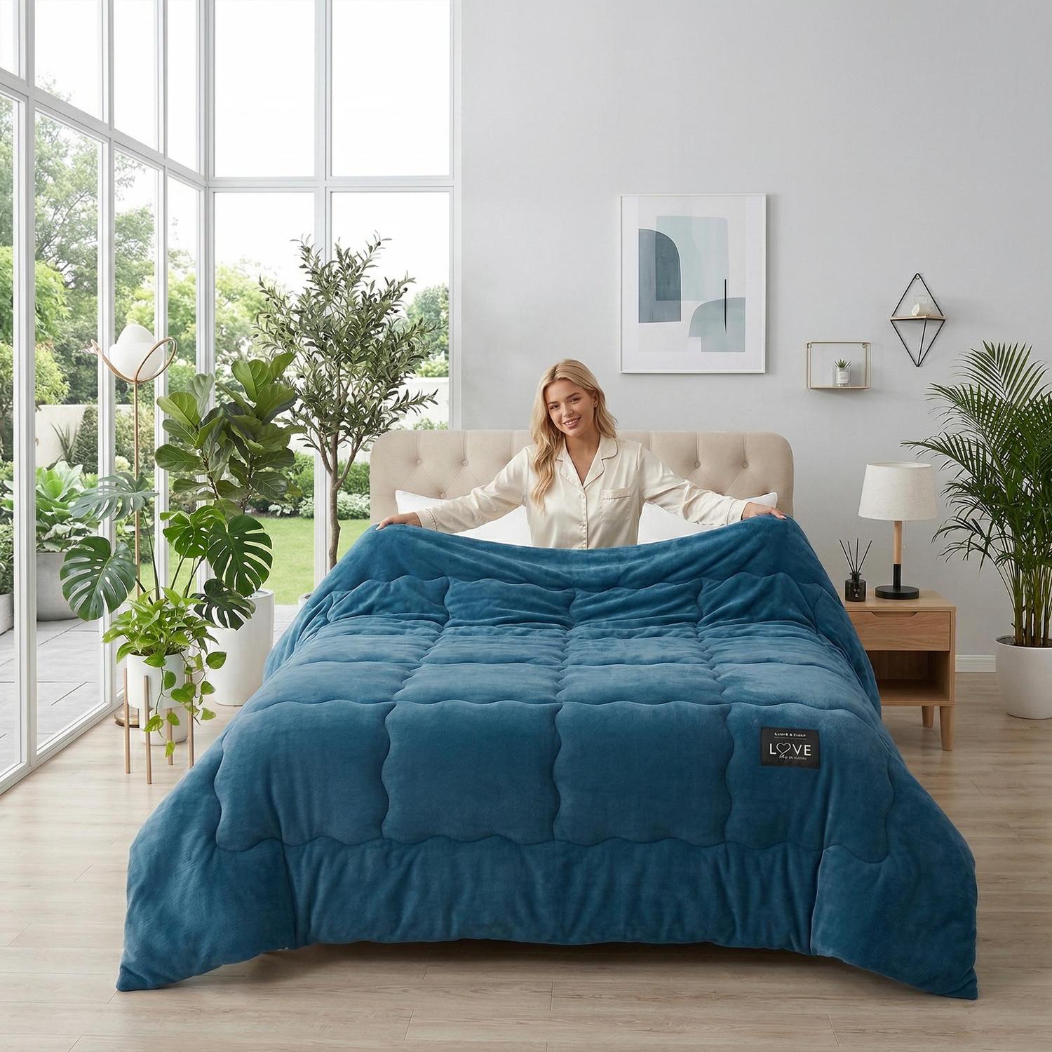 Woman in bed holding up a soft, plush blue quilted blanket with a "LOVE" tag.