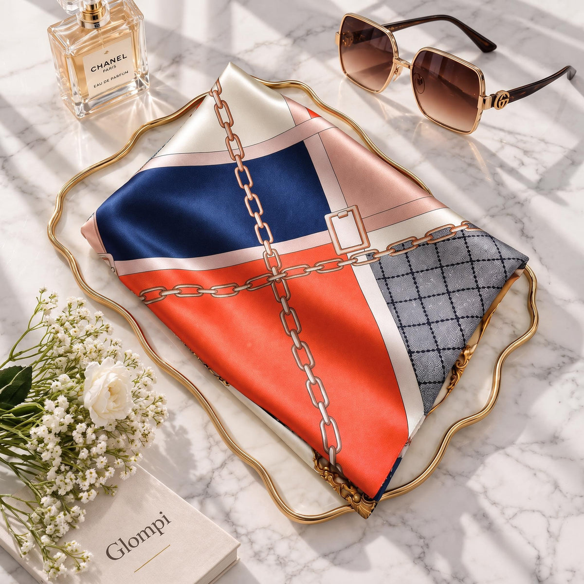 100% mulberry silk scarf featuring an orange, blue, and cream chain link grid pattern on a gold tray with accessories.