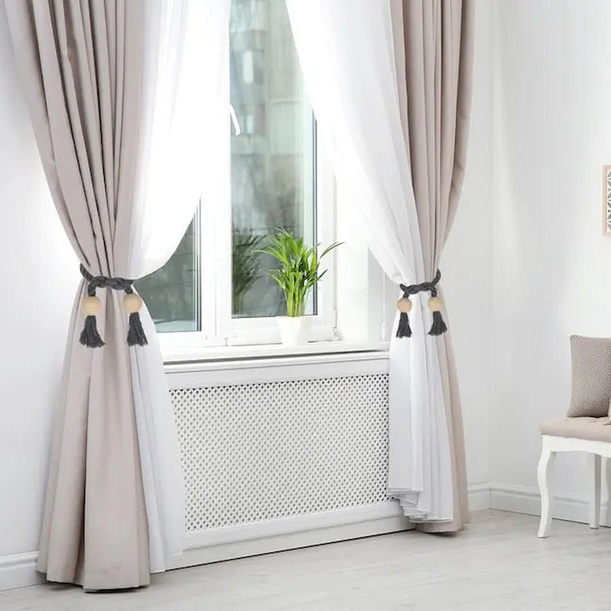 Grey braided magnetic curtain tiebacks with wooden beads and tassels holding back beige and white curtains.