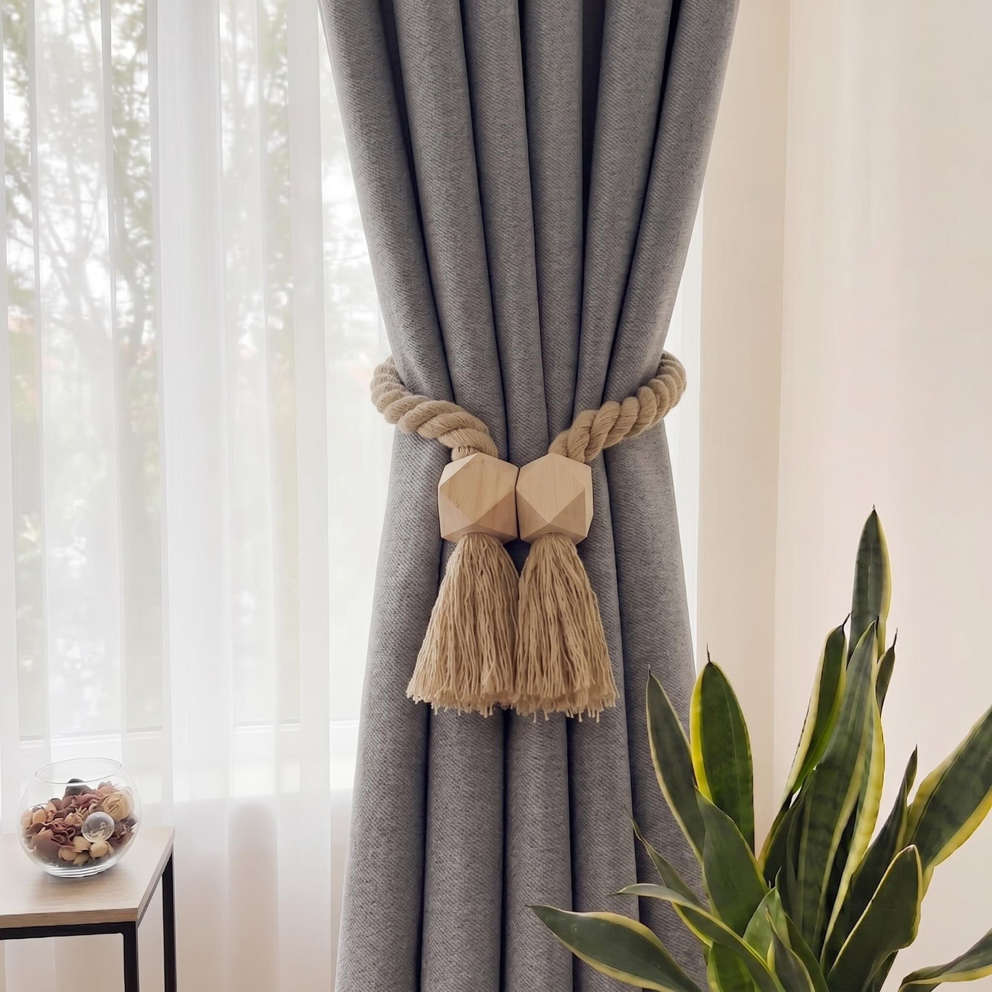 Beige cotton rope curtain tieback with geometric wooden beads and tassels on a grey curtain.