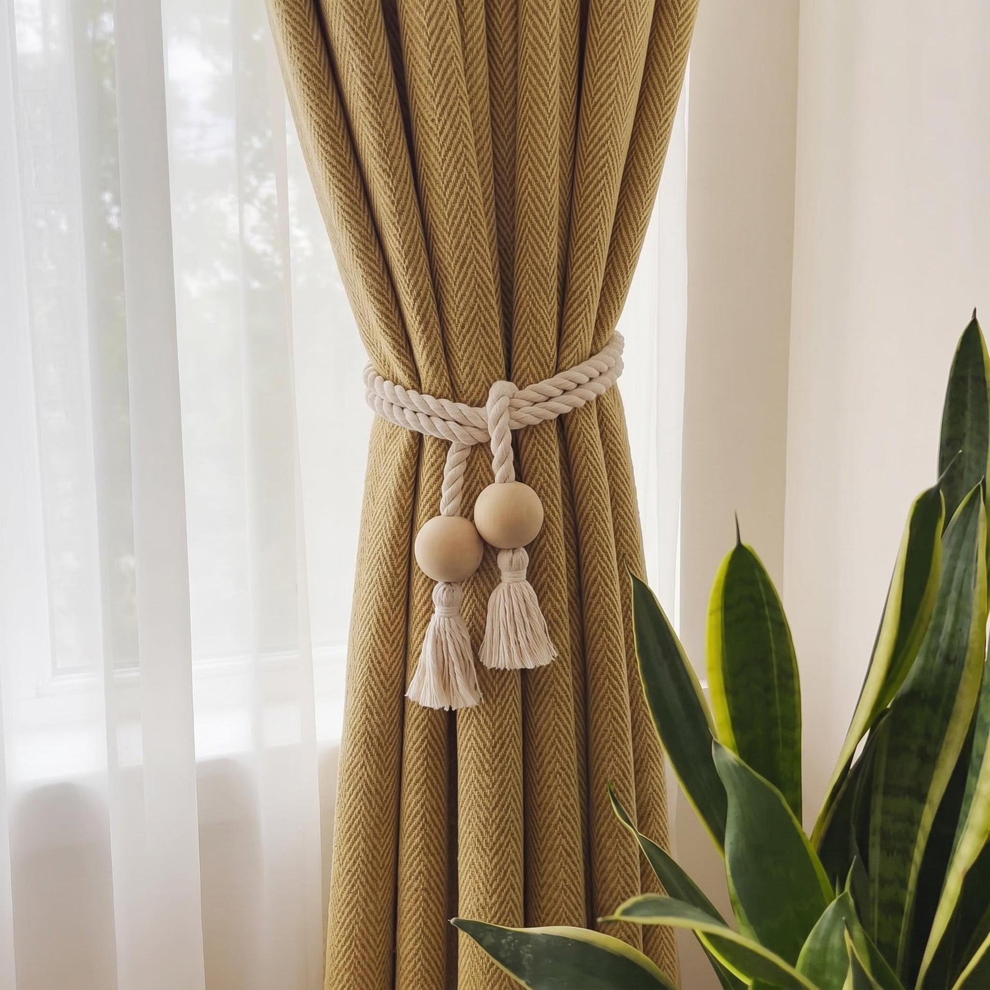 Boho wooden bead and white cotton rope curtain tieback with tassels on a yellow textured curtain.