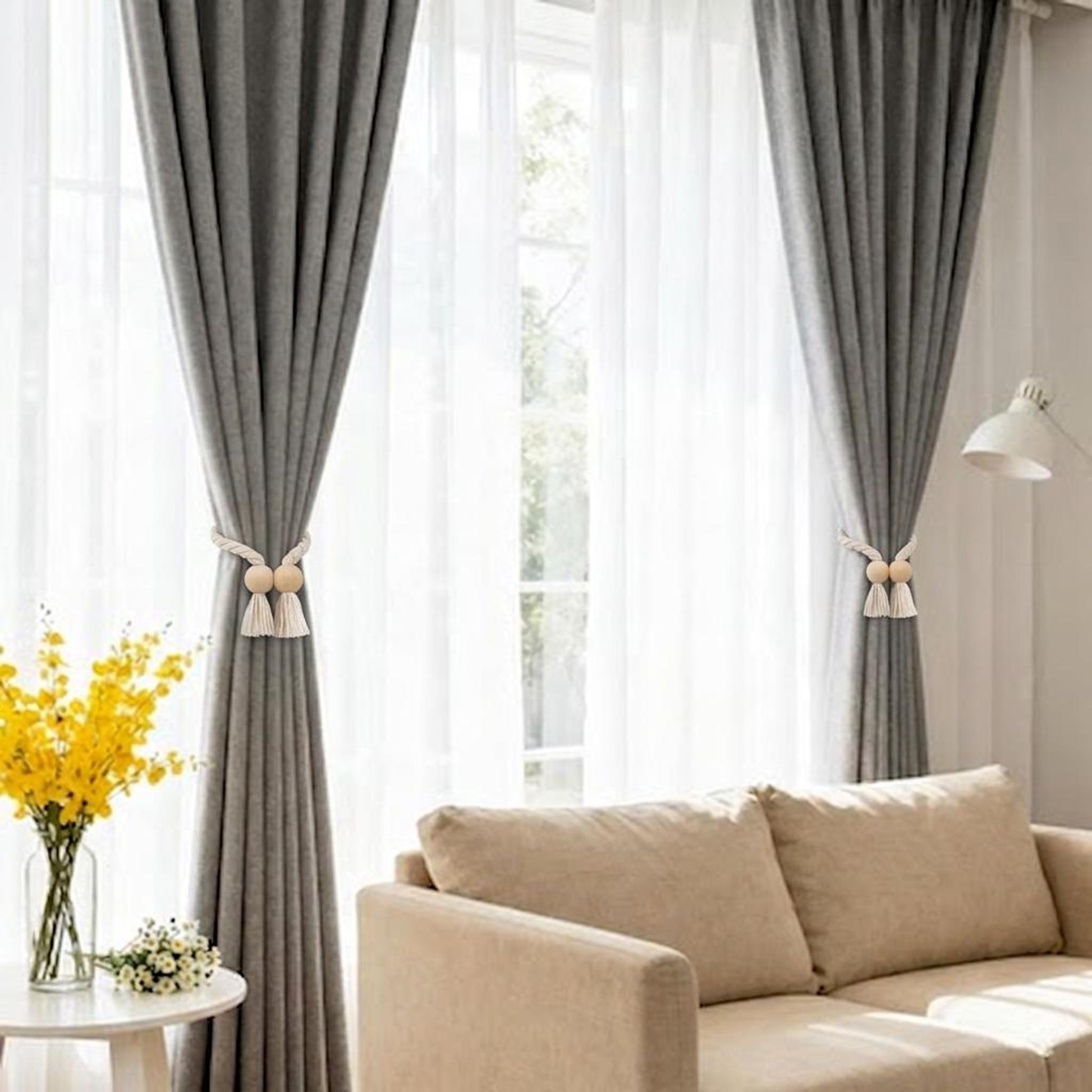 Wooden bead curtain tiebacks with white cotton tassels holding back grey drapes in a living room.