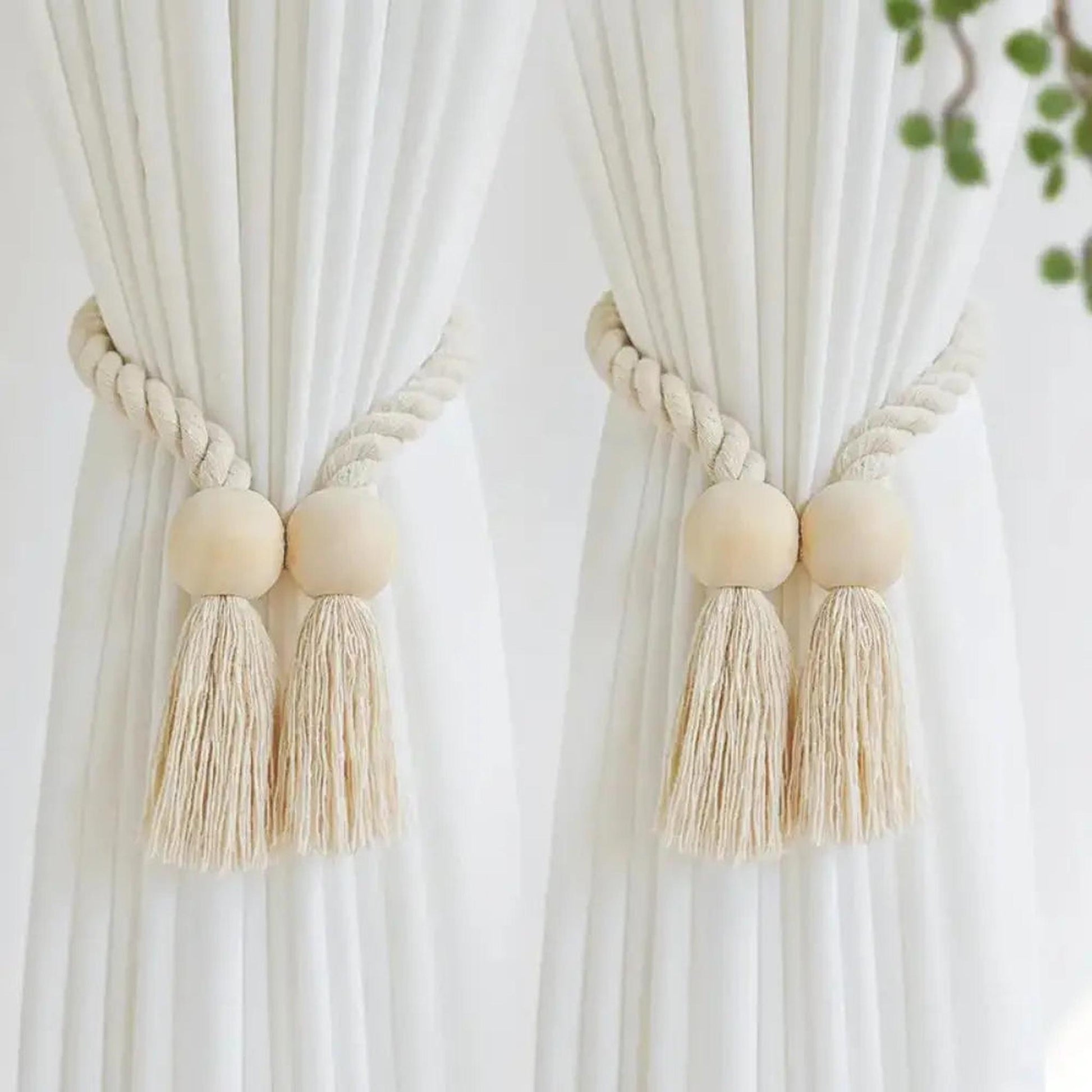 Two beige cotton rope curtain tiebacks with wooden beads and tassels holding white curtains.
