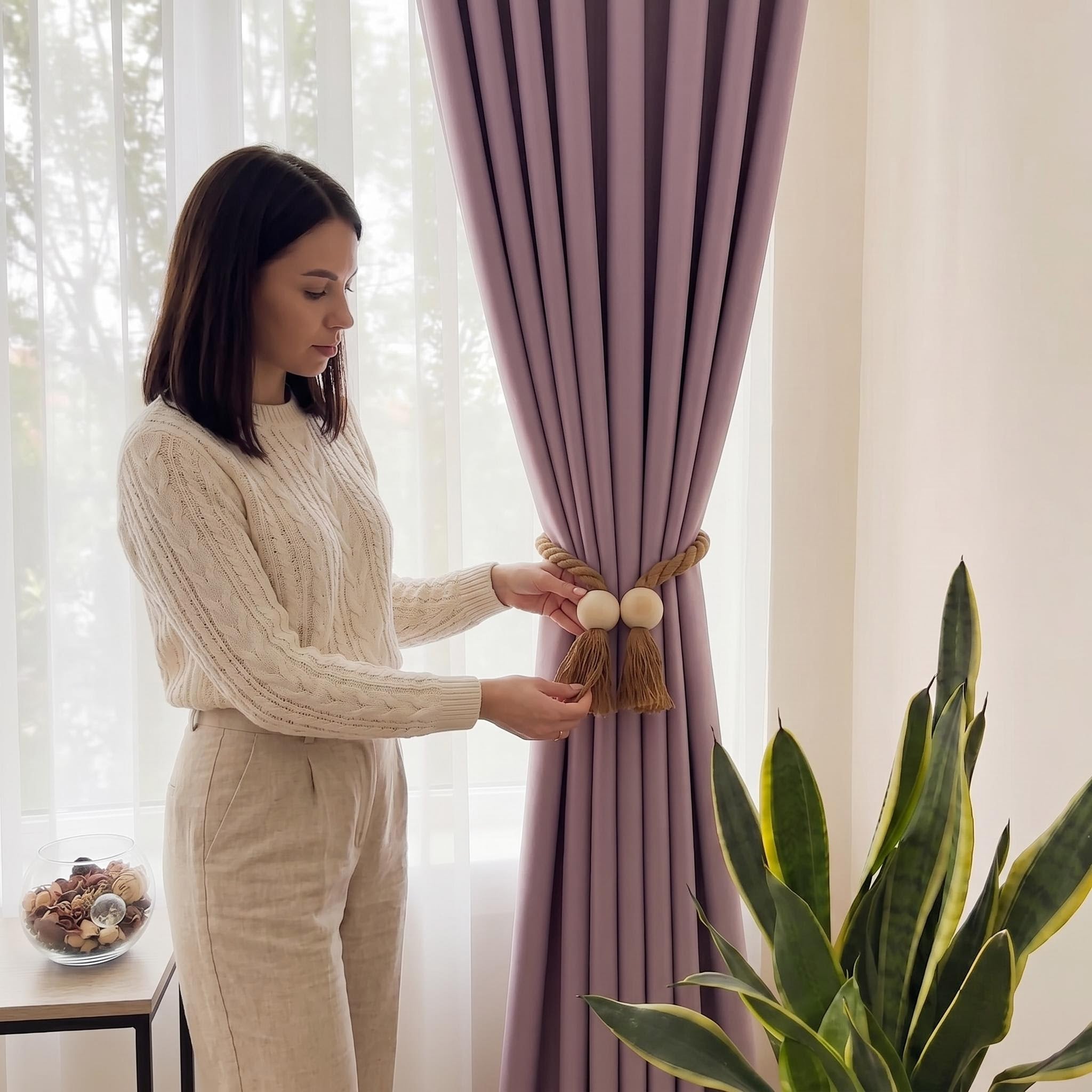 Woman styling purple curtains with a wooden bead magnetic tieback and cotton tassel.