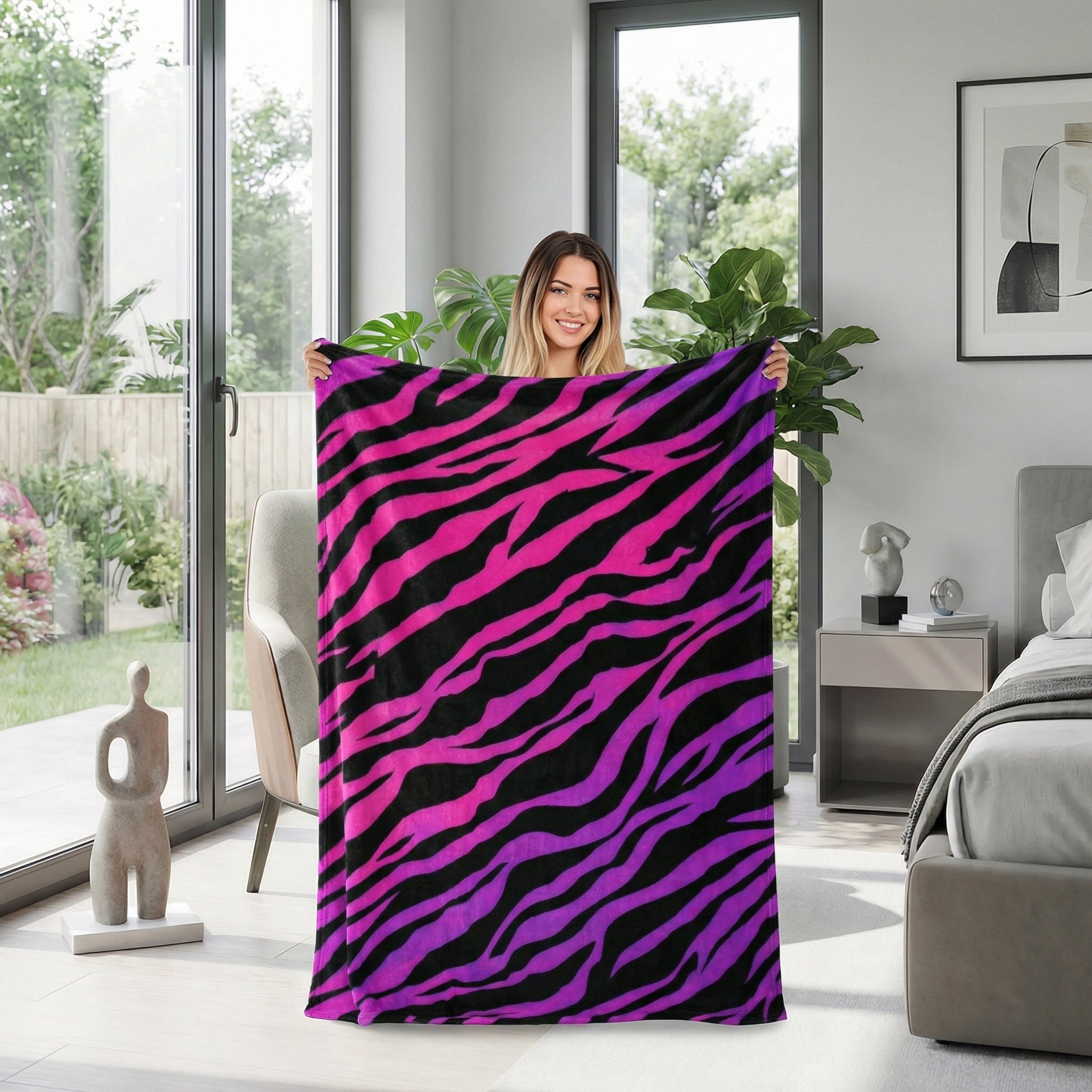 Smiling woman holding a vibrant pink and purple zebra pattern flannel blanket in a modern room.