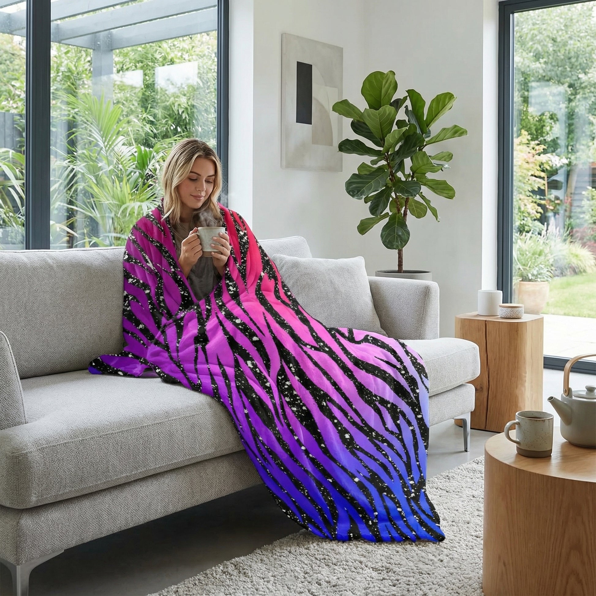 Woman on a sofa wrapped in a vibrant pink, purple, and blue ombre zebra pattern flannel blanket.