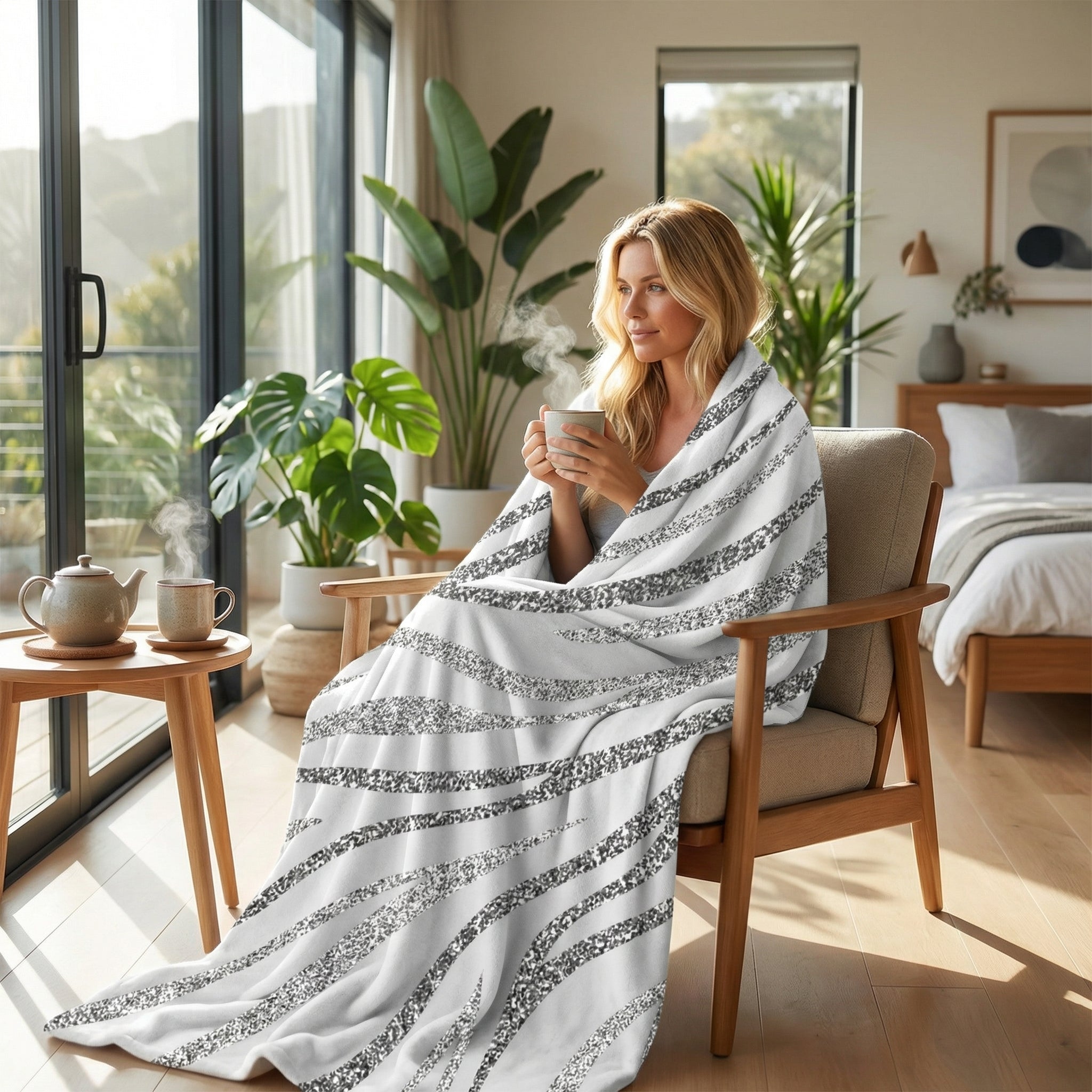 Woman wrapped in a soft white flannel blanket with shimmering silver zebra stripes, enjoying a hot drink indoors.